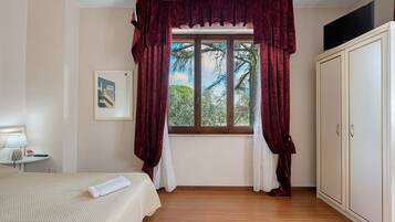Habitación de hotel con cama, ventana con cortinas, armario y un cuadro en la pared.