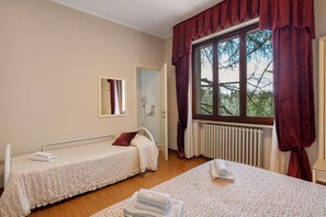Ein Zimmer mit zwei Einzelbetten, einem fenster mit Vorhängen, einem Heizkörper und einem Spiegel an der Wand.