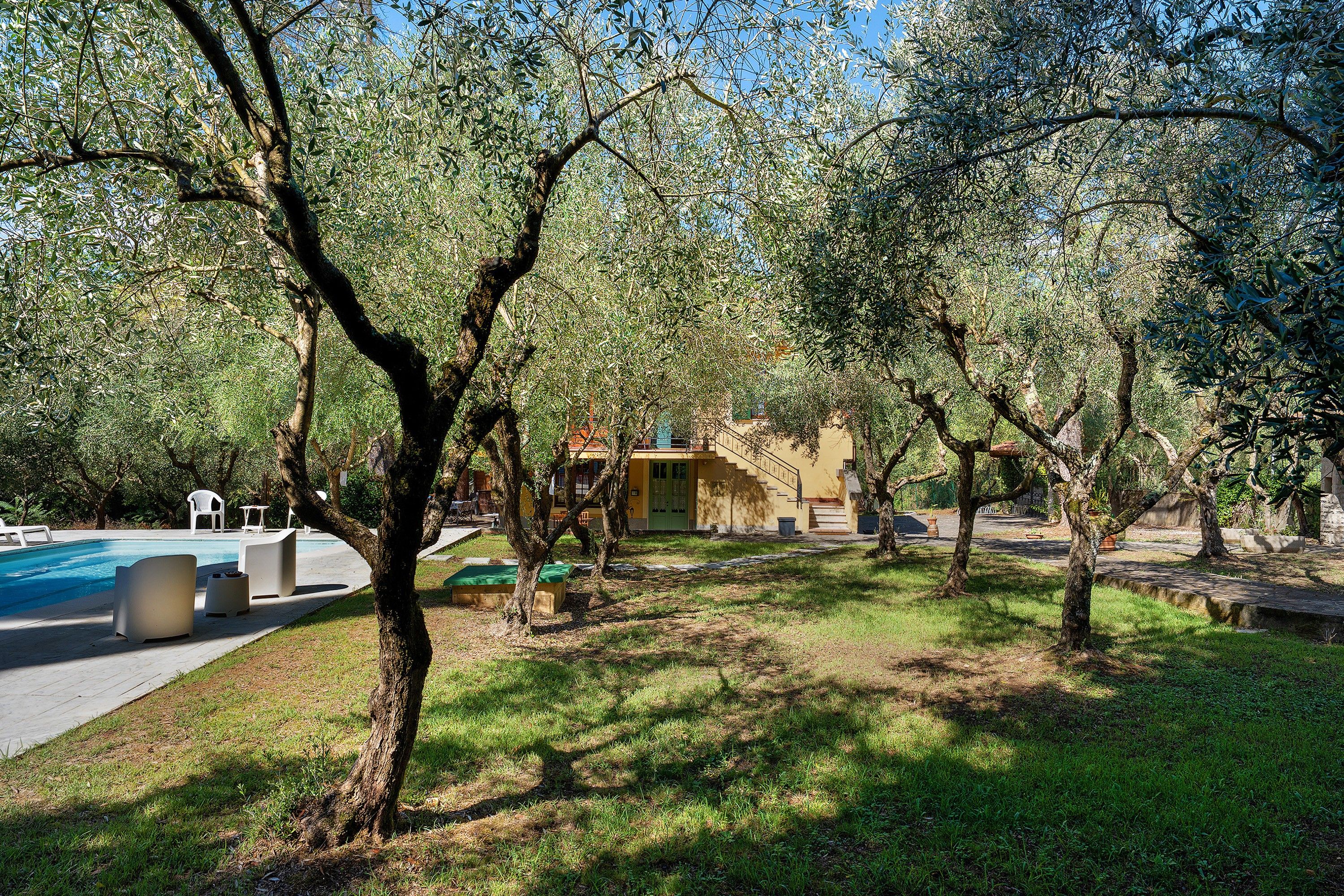 Area piscina sotto un cielo sereno, circondata da alberi e un edificio con facciata gialla.