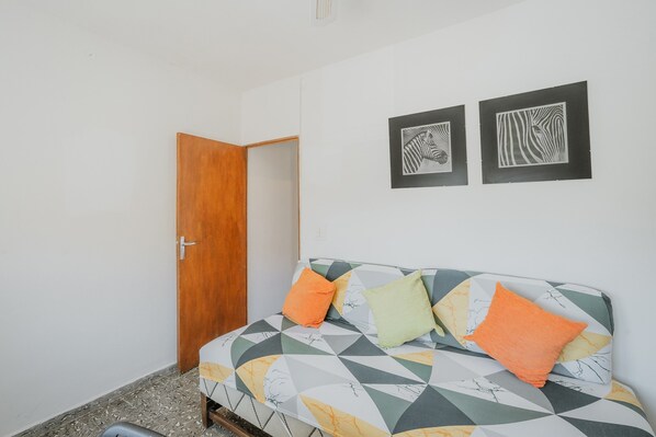 A room with a wooden door, a sofa with patterned cushions, and two framed artworks on the wall. - Vacation Home 'Pisito De Pueblo II' with Mountain View, Wi-Fi, and Air Conditioning (Navaluenga)