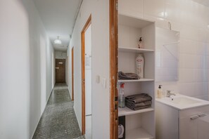 A hallway with a white sink, shelves with toiletries, and a door at the end. - Vacation Home 'Pisito De Pueblo II' with Mountain View, Wi-Fi, and Air Conditioning (Navaluenga)