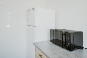 A kitchen with a white refrigerator, a black microwave, and a wooden cabinet. - Vacation Home 'Pisito De Pueblo II' with Mountain View, Wi-Fi, and Air Conditioning (Navaluenga)