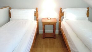 Een kleine, eenpersoonskamer met twee eenpersoonsbedden, een houten nachtkastje en een bijzettafeltje met een lamp.