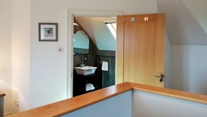 Een kamer met een houten deur, een lijst met een afbeelding aan de muur en uitzicht op een badkamer met een wastafel en handdoekhouder.