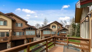 A wooden deck with metal chairs, a stone wall, and a view of multiple houses. - Great Savings for Labor Day! A/C, Hot Tub, 2 En suites (Steamboat Springs)