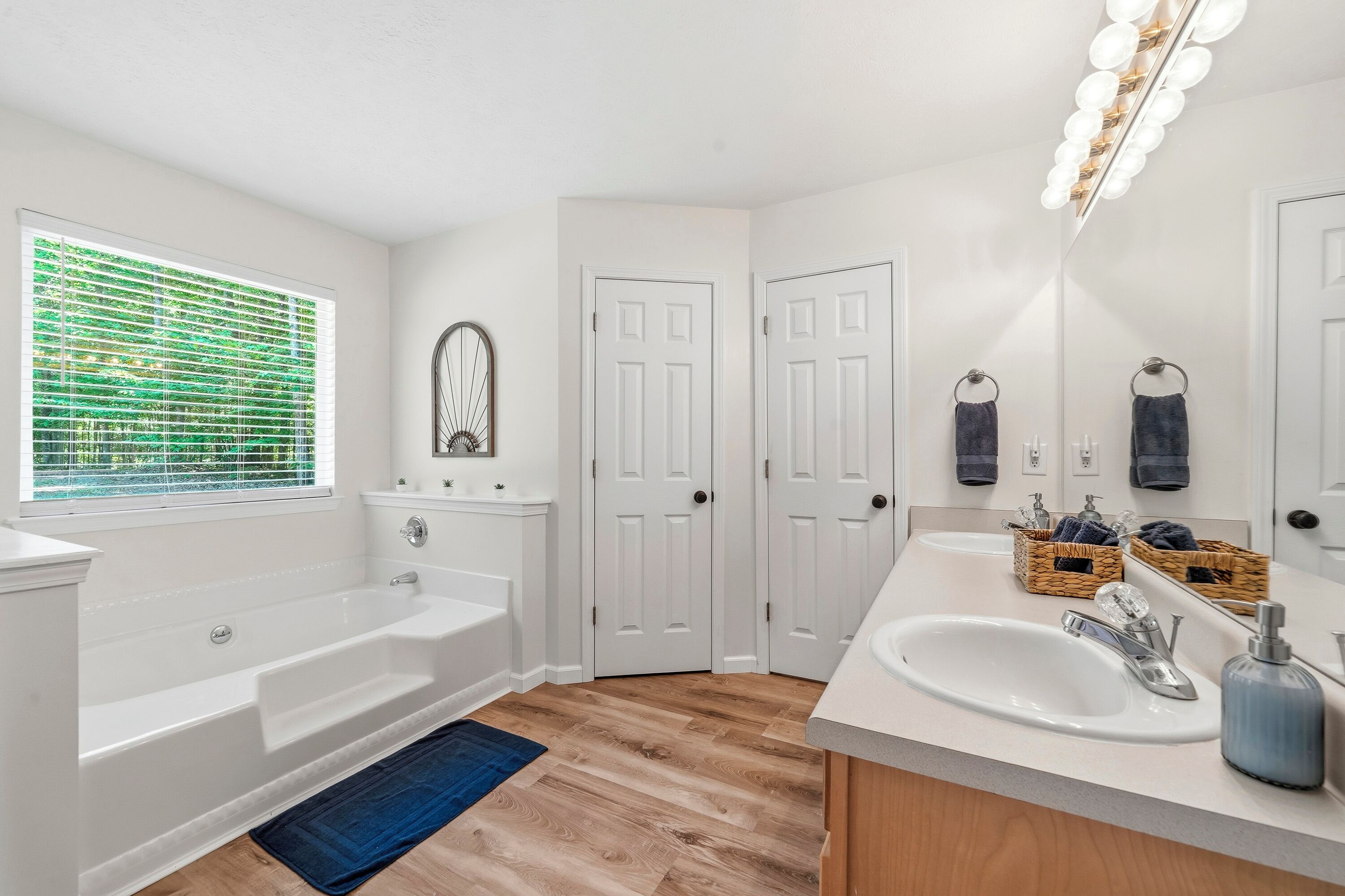 A bathroom with a bathtub, a sink, a mirror, and a window with blinds.