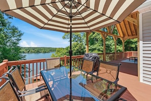 Une terrasse avec une table et des chaises en verre, un parasol à rayures et une vue sur un lac.