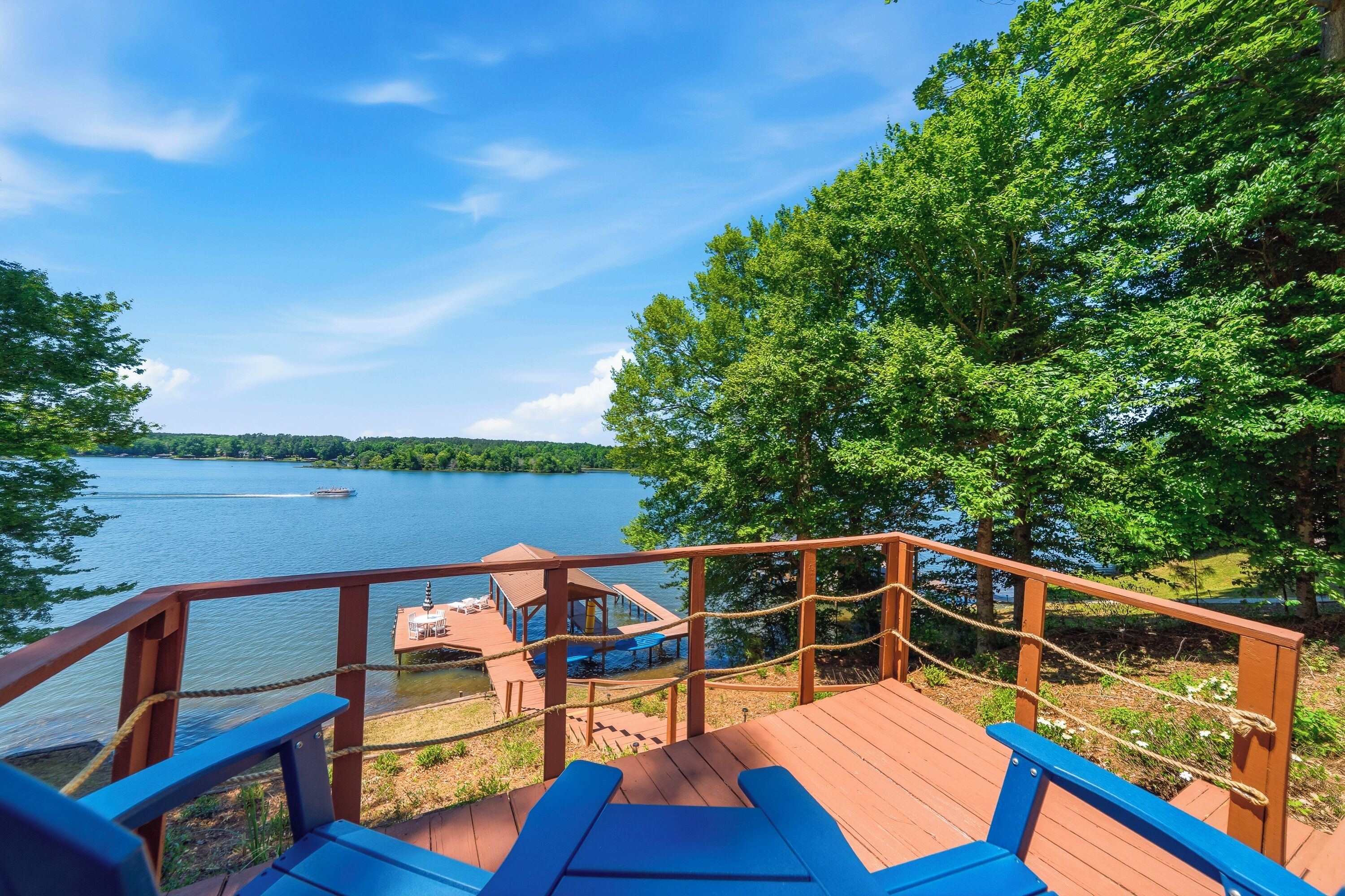 A wooden deck with blue chairs overlooking a lake, a dock, and a small building.