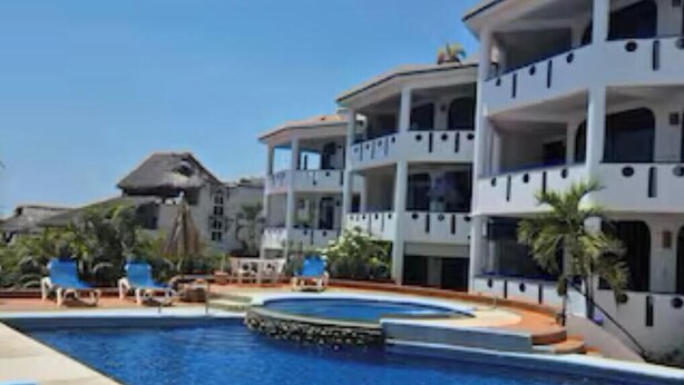 A hotel with a swimming pool, multiple balconies, and lounge chairs.