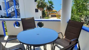 A balcony with a round table and four chairs, overlooking a coastal area with buildings and a view of the sea.