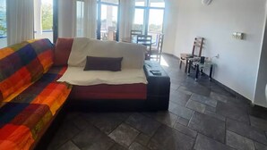 A room with a sofa, a bed, a ceiling fan, and large windows.