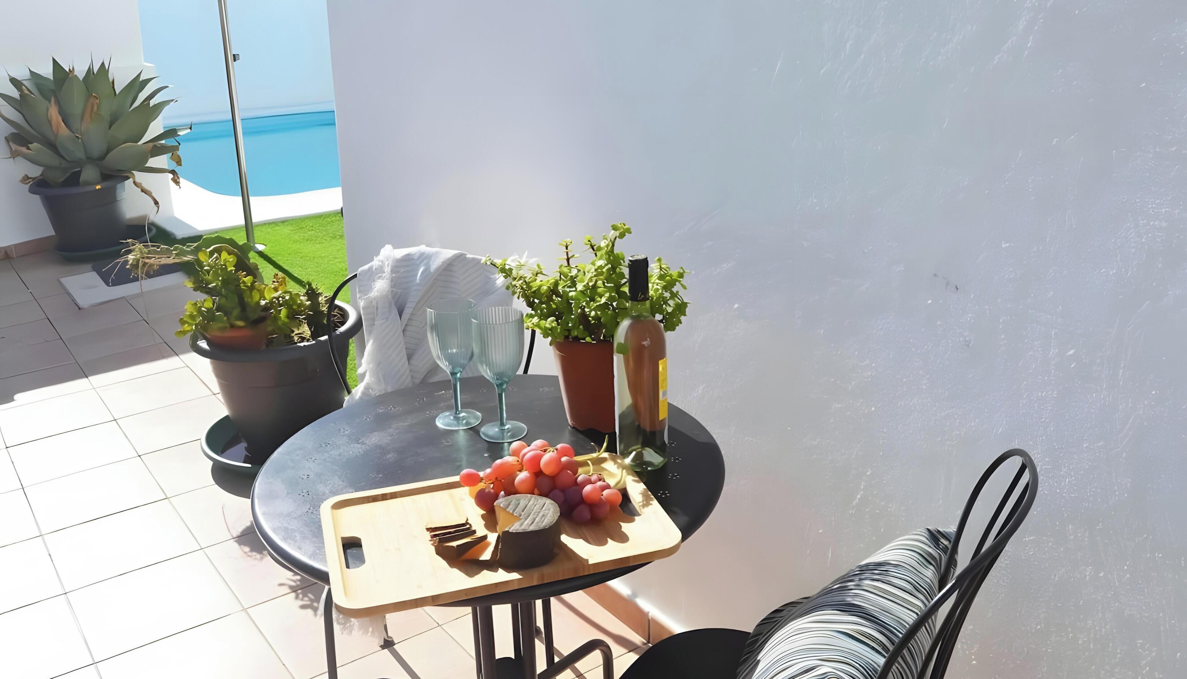 A patio with a table set for a meal, including a cutting board, grapes, and a bottle.