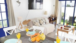 Un comedor con una mesa dispuesta para el desayuno, que incluye platos, cubiertos y un frutero con naranjas y plátanos.
