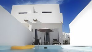 Een modern gebouw met een zwembad, een gele ligstoel en een overdekt terras met een stoel.
