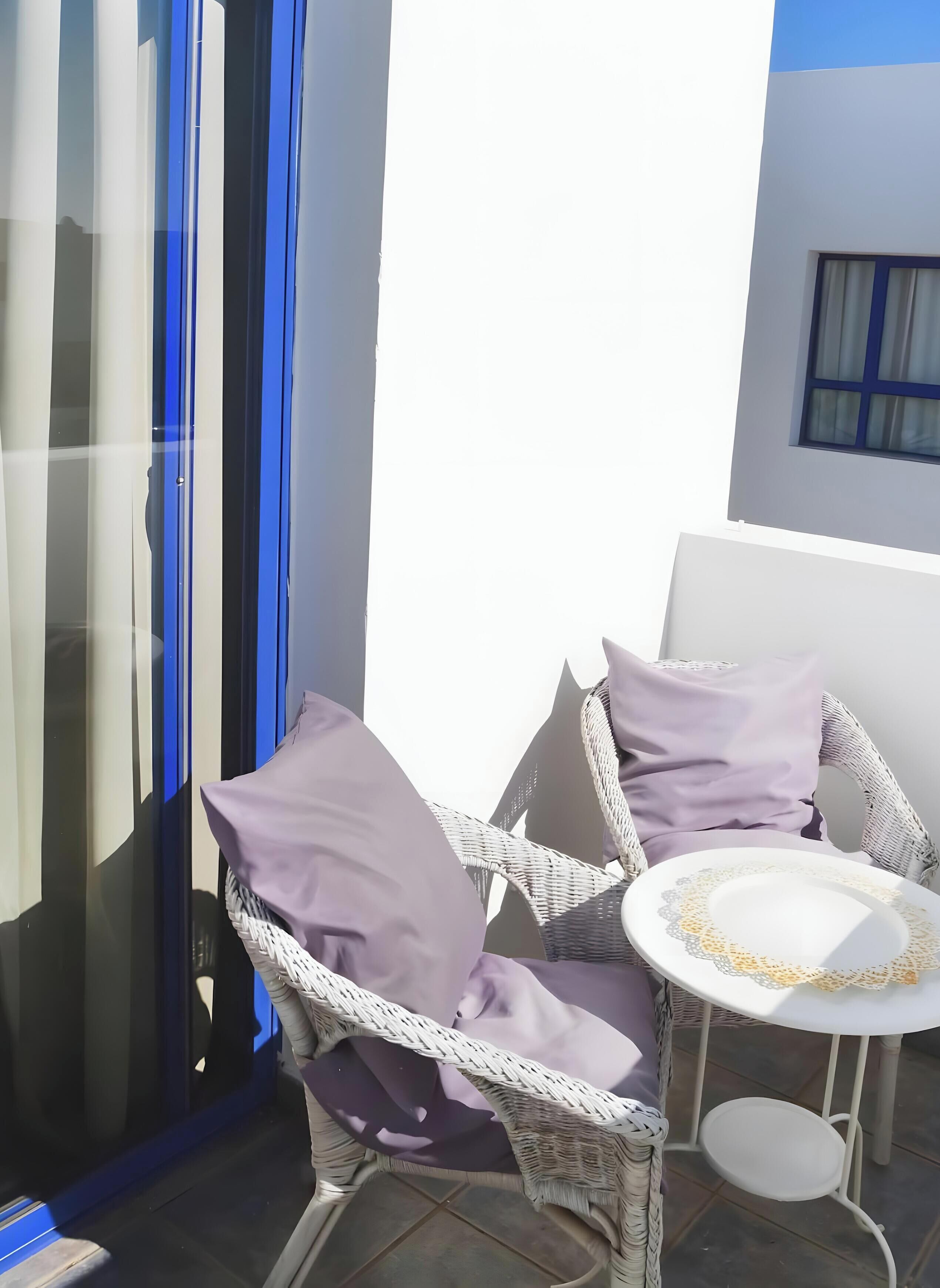 A wicker chair with cushions, a small round table with a lace doily, and a glass door with blue accents.