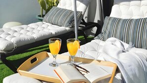 Un espacio al aire libre con luz solar, con dos sillones, una mesa con bandeja y un libro.