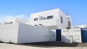Un edificio moderno blanco con techo plano, un pequeño balcón y una puerta con marco azul.