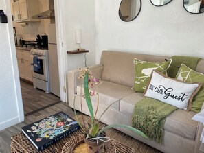 A living room with a beige sofa, a travel book, a potted orchid, and a 'BE OUR GUEST' pillow. - Pet Friendly Private Unit with Fully Fenced Patio (Long Beach)