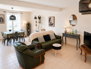 Ein Wohnzimmer mit einer Couch, einem Esstisch, Stühlen, einem Fernseher, einer Lampe und einem Spiegel.