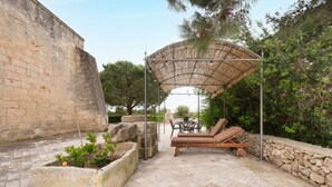 En uteplats med en pergola, solstolar och en stenmur.