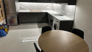 Moderni keittiö, jossa on sisäänrakennettu pesukone, jääkaappi ja ruokailutila pyöreän pöydän ympärillä.