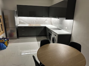 Moderni keittiö, jossa on sisäänrakennettu pesukone, jääkaappi ja ruokailutila pyöreän pöydän ympärillä.