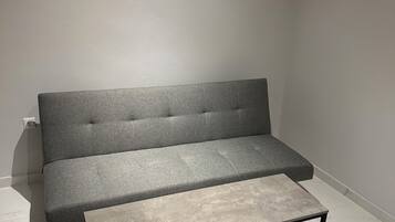 A grey sofa with a wooden bench in front, a black metal frame, and a white marble floor.