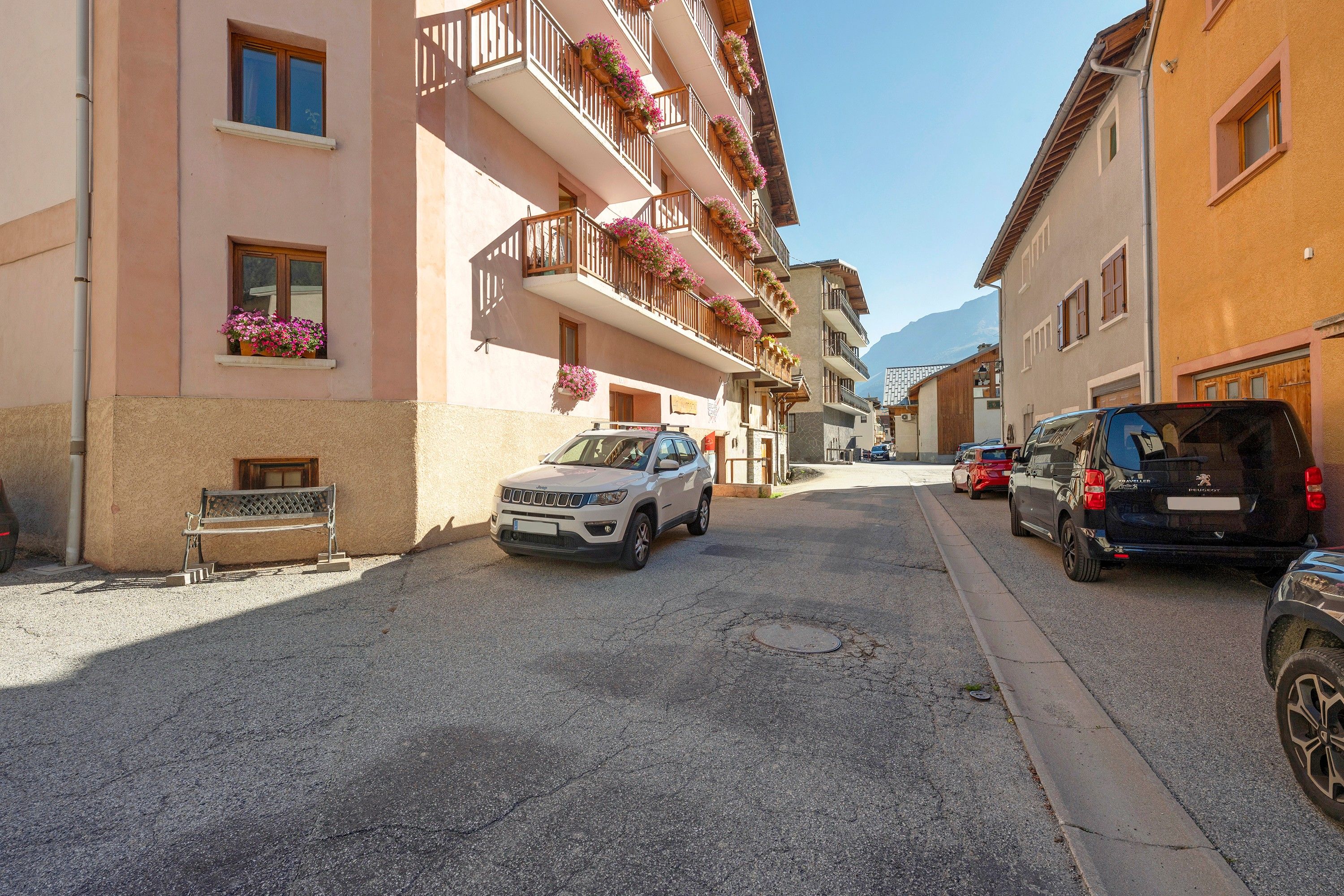 A street with parked cars and a building with balconies adorned with flowers.