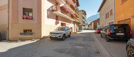 A street with parked cars and a building with balconies adorned with flowers.