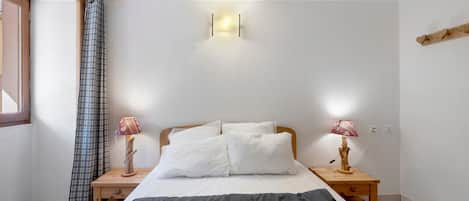 Un dormitorio con una cama, dos mesitas de noche con lámparas, una ventana con cortinas y una lámpara de pared.