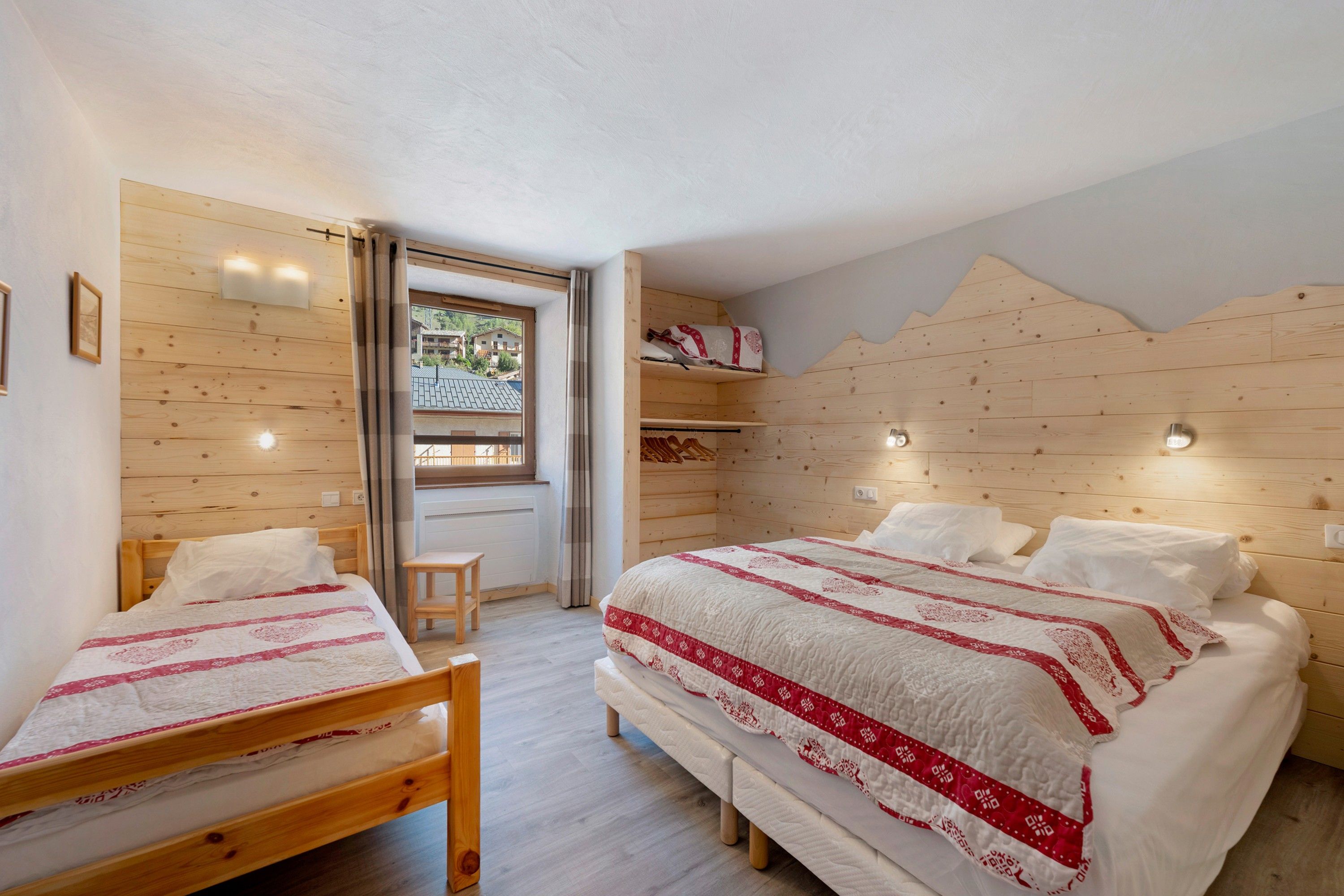 Une chambre avec deux lits en bois, une fenêtre donnant sur un beau paysage et une tête de lit en bois.