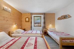 Et værelse med to træsenge, et vindue med udsigt til et hus, og en trævæg med et spejl og billedrammer.