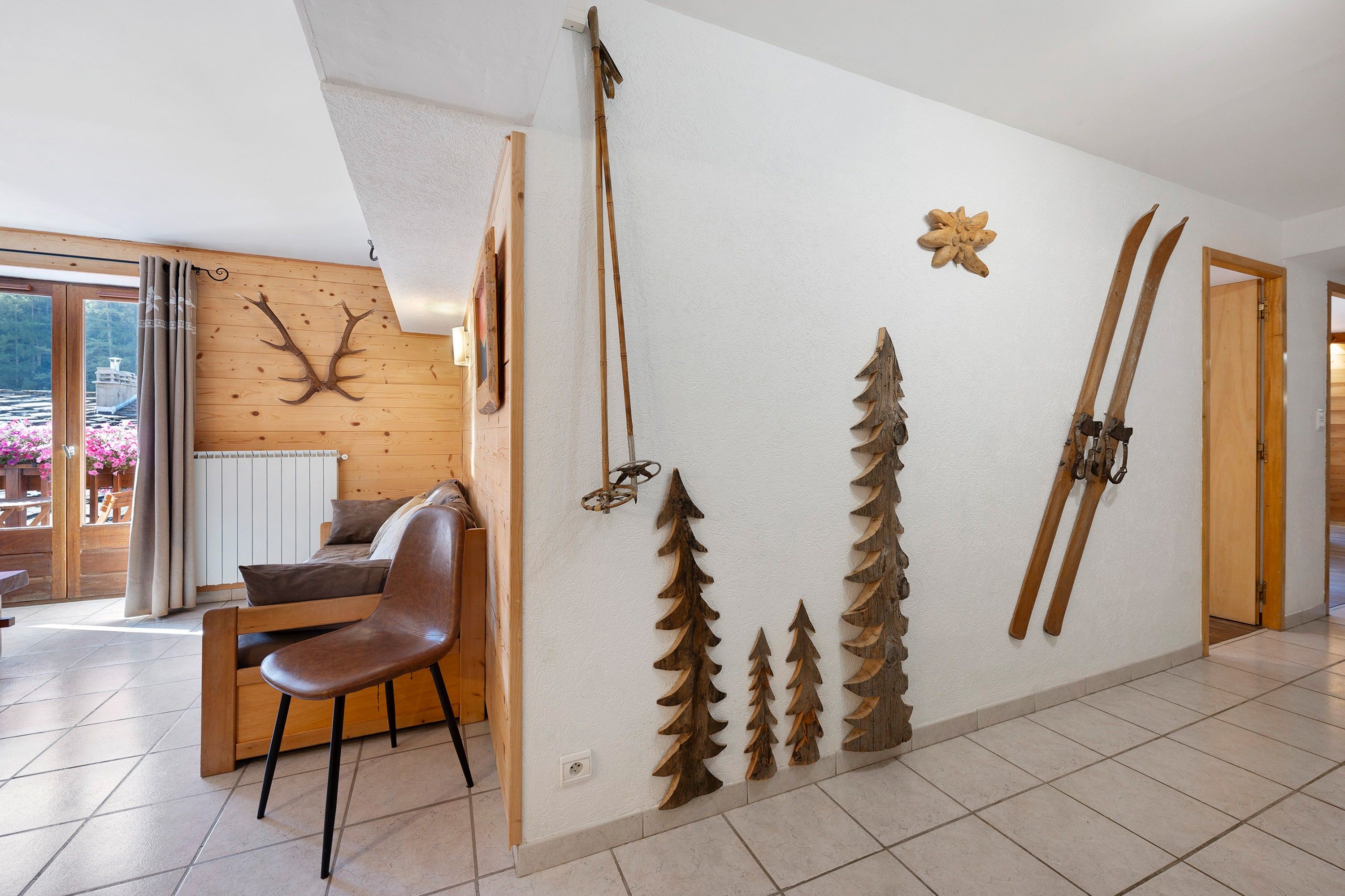 A room with a wooden wall, a dining area with a chair, and a view of a forest through a window.