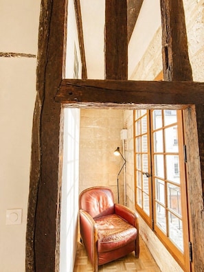 A room with exposed wooden beams, a leather chair, a floor lamp, and a view through large windows.
