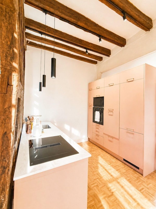 A kitchen with a central island, wooden beams, pendant lights, and a built-in oven.
