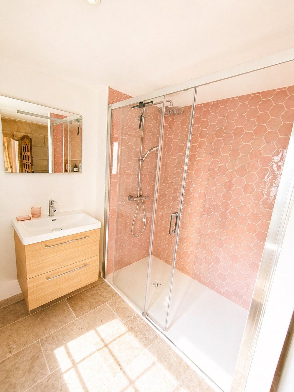 A bathroom with a glass-enclosed shower, a white sink with a mirror above it, and a wooden vanity.
