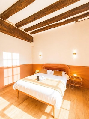A bedroom with a wooden ceiling, a bed with white bedding, two bedside tables with lamps, and a window with blinds.