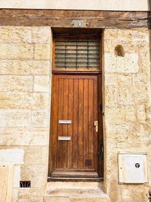 Une porte en bois avec une plaque en métal portant un numéro, une petite fenêtre à carreaux et une sonnette en métal.