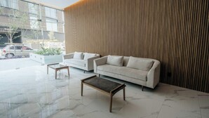 Eine moderne Lobby mit einem weißen Sofa, zwei Beistelltischen und einer Wand aus Holzlatten.