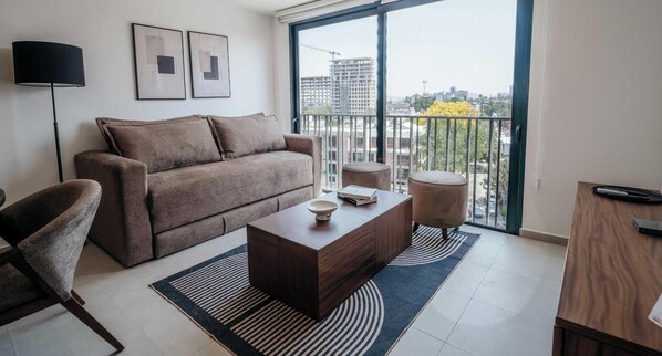 A modern living room with a sofa, coffee table, and a view of the city through a balcony.