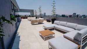 Eine Dachterrasse mit moderner Außenlounge, darunter eine Sofagruppe und ein Holztisch.