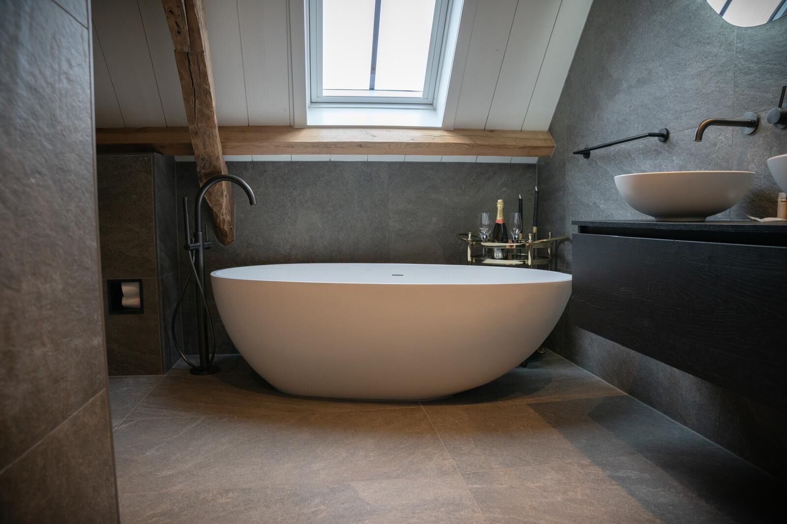 A modern bathroom with a freestanding bathtub, a large mirror, and a skylight.