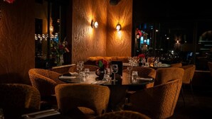 A dimly lit restaurant with a long table set for dining, surrounded by patterned chairs. - Room4 (Maurik)