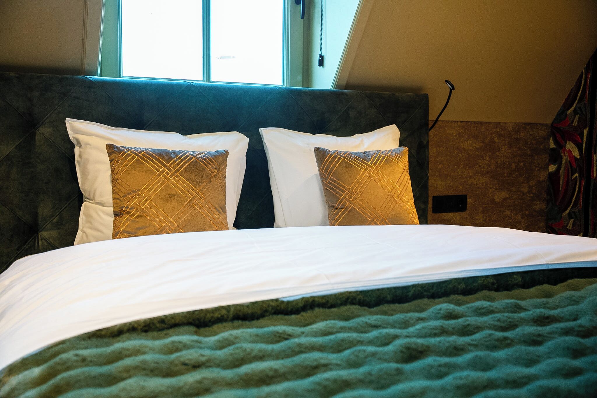 A bed with white and patterned pillows, a green textured bedspread, and a window with daylight.