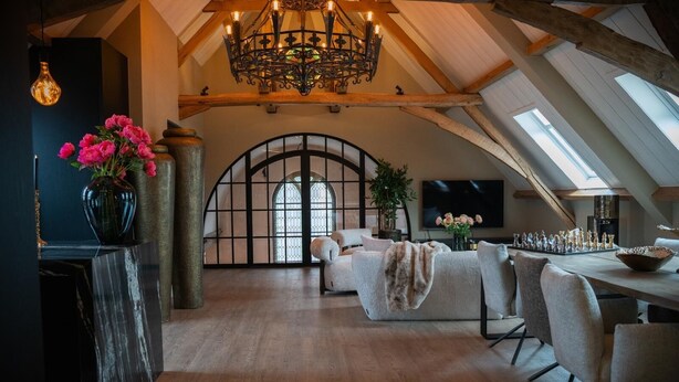 A spacious loft with a high ceiling, a chandelier, a dining area with a chessboard, and a large arched window. - Room4 (Maurik)