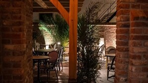 An outdoor patio area with brick walls, wooden beams, and tables with chairs. - Room4 (Maurik)