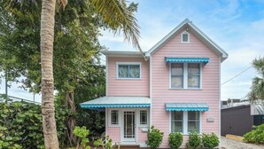 Et pink hus med to etager, med markise i blå, en veranda og et lille haveområde.