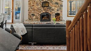 Una sala de estar acogedora con chimenea de piedra, vigas de madera en el techo y vistas a través de un ventanal.