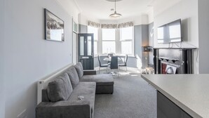 A modern living room with a sofa, dining table, chairs, and a TV. - Cosy 2-Bed apartment | sleeps 6 | Sea views - Pass the Keys (Southend-on-Sea)