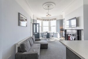 A modern living room with a sofa, dining table, chairs, and a TV.